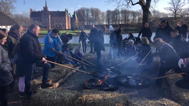 Folk bager pandekager over bål